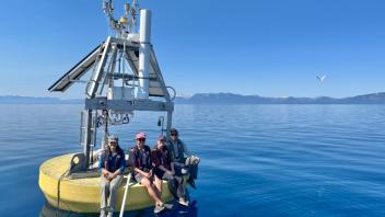 Yellow ocean buoy with five people sitting on calm blue water, mountains on horizon