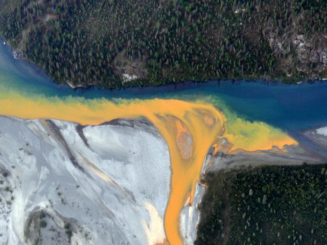 Arial photograph of an orange stream entering a pristine stream in Alaska. 